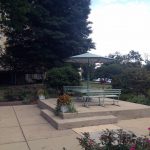 Canopied bench and table, on concrete riser, around maintained grounds